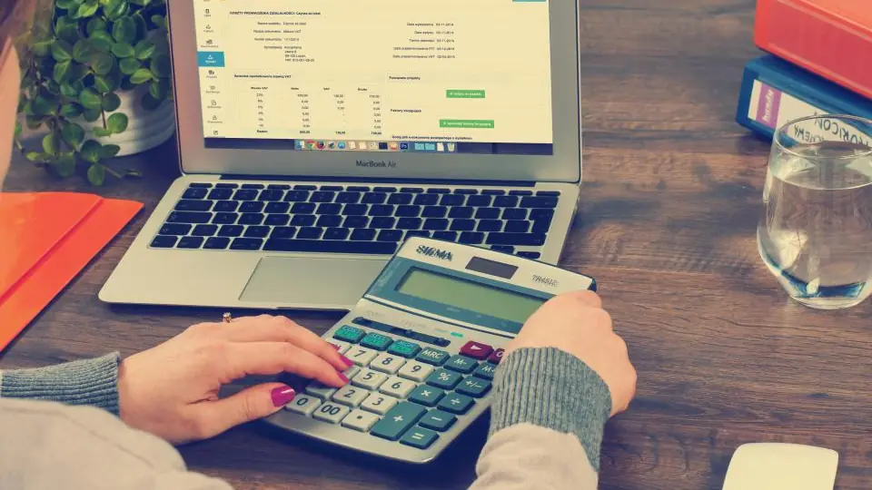 Accountant using a calculator next to a spreadsheet on a laptop