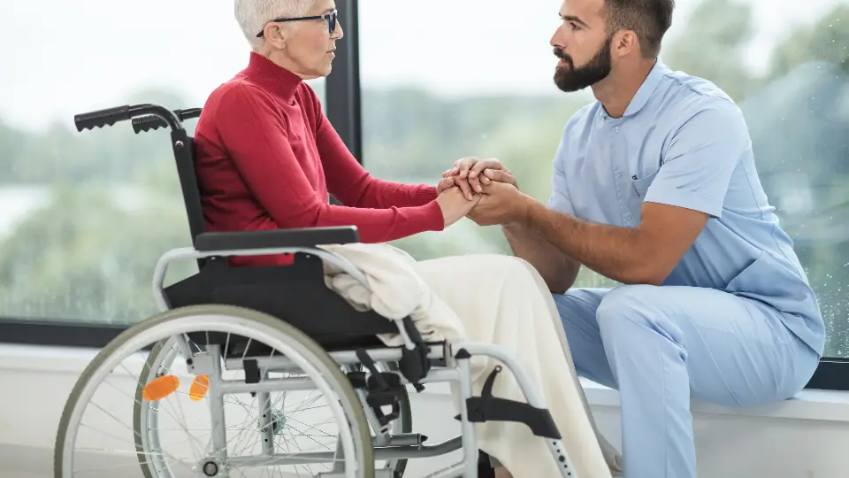 Aged care worker talking with a smiling older woman in a wheelchair