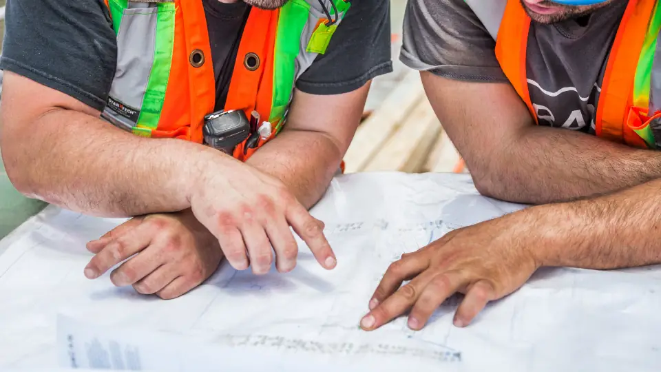 Construction workers in hi-vis vests reviewing building plans