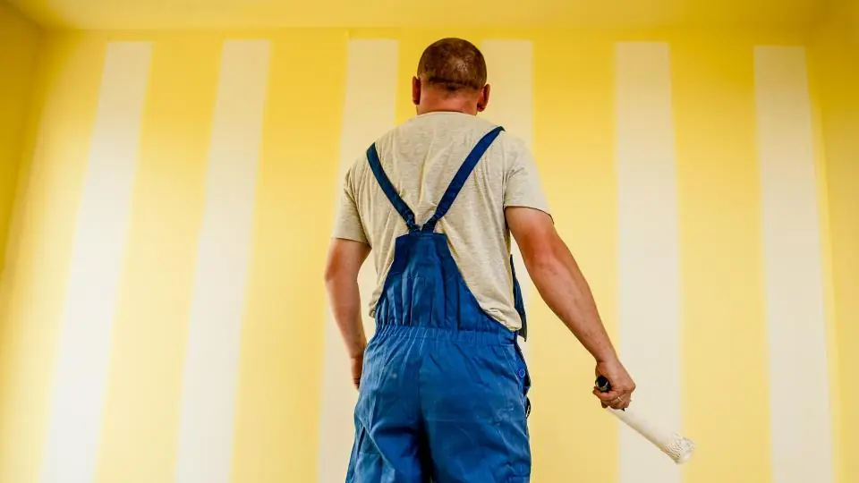 Painter in overalls holding a brush in front of a freshly painted wall