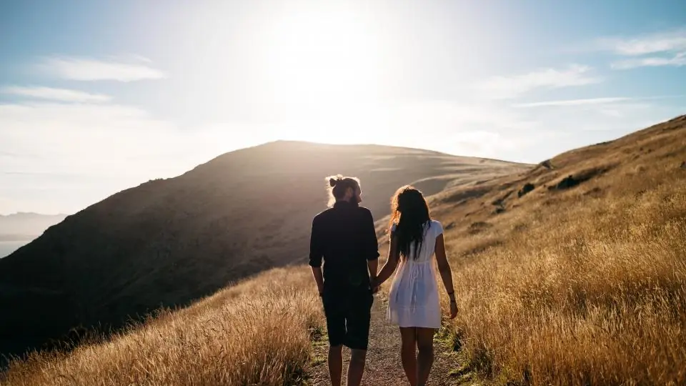 Couple walking hand in hand up a grassy hill at sunset