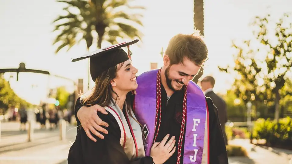 Two university graduates in gowns celebrating after their graduation ceremony