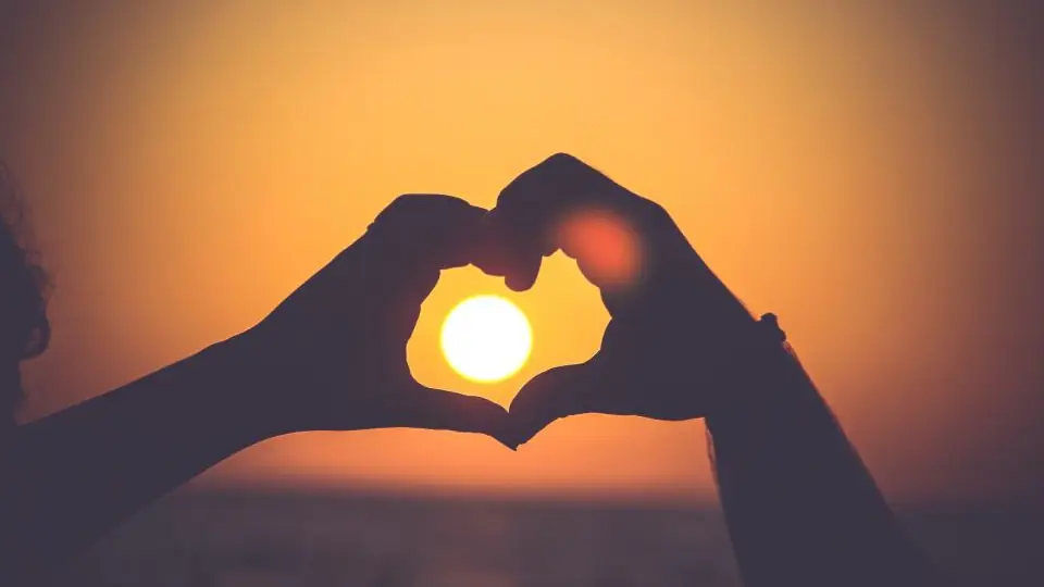 Hands forming a heart shape against a glowing sunset