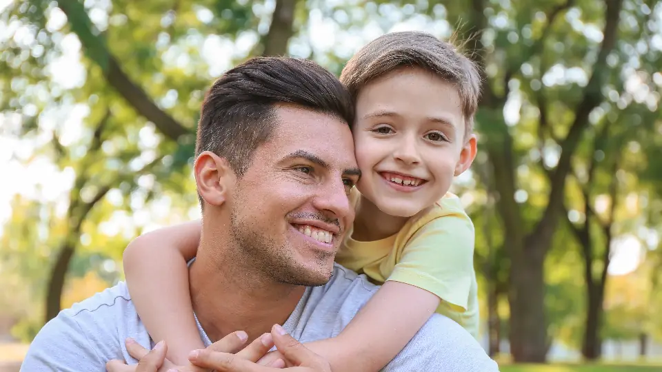 Father and young son smiling together outdoors in a park