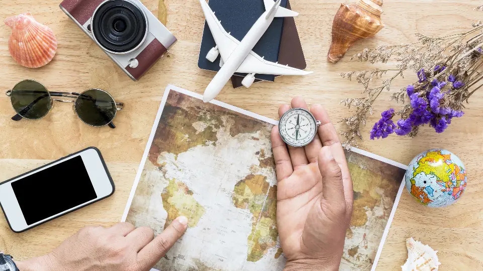 Hands planning travel on a world map with a compass and phone