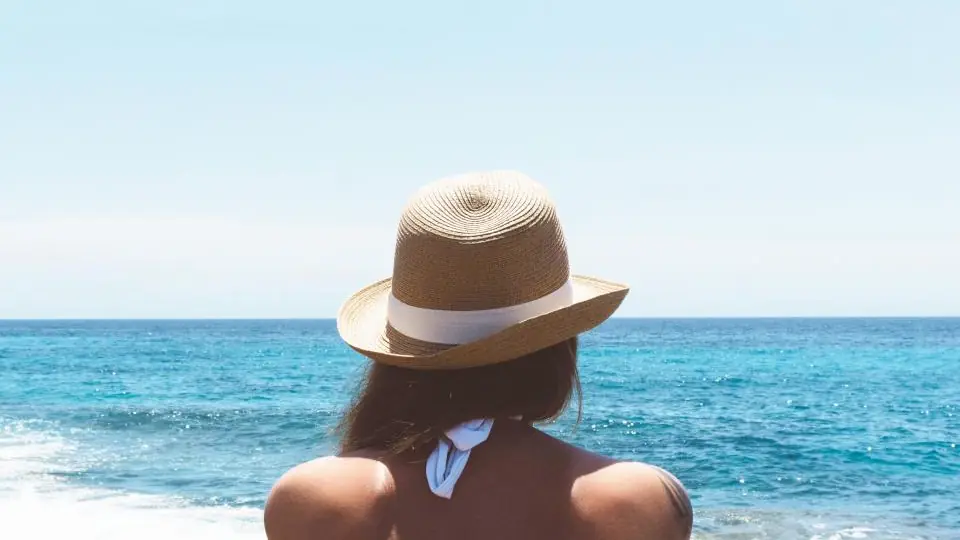 Traveller in a sun hat looking out over a blue ocean